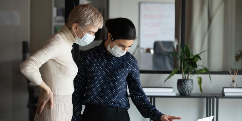 Two women in masks looking at a computer