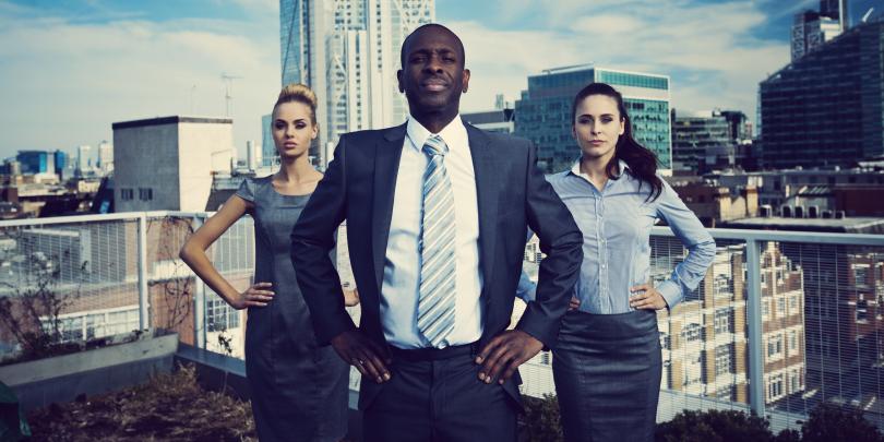 Three businesspeople posing like superheroes on a roof