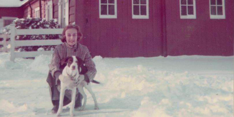 Marilyn Rogers Becker and her dog, Molly outside in snow by red house